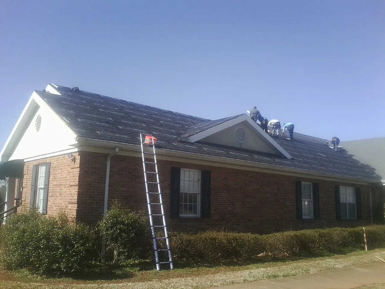 Crew tearing shingles off a brick ranch roof with a ladder set — Metal Roof Repair work by our crew in Townsend