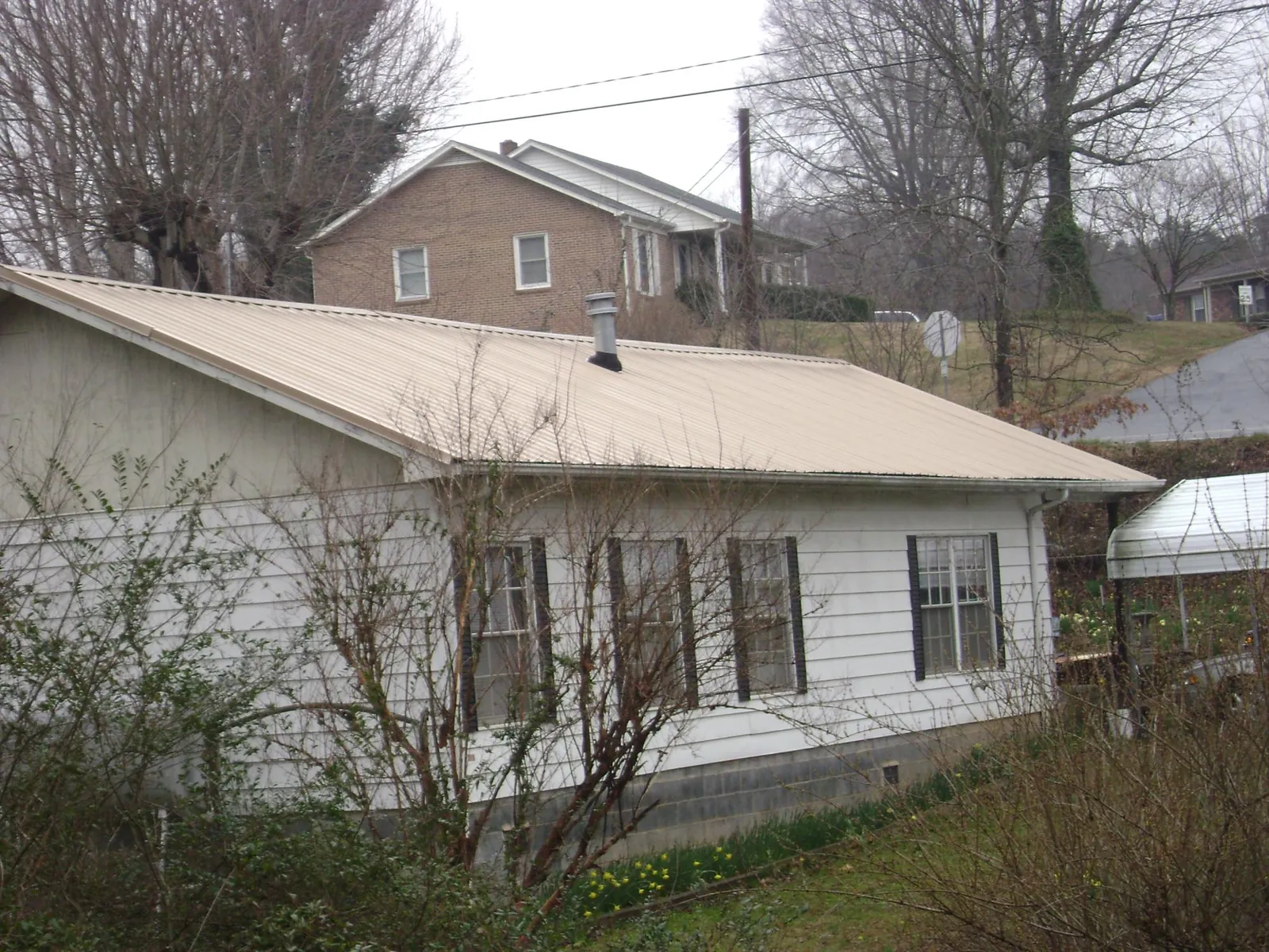 Tan metal roof on a white sided house set into a hillside — Commercial Roofing by Roofing Brothers in Townsend